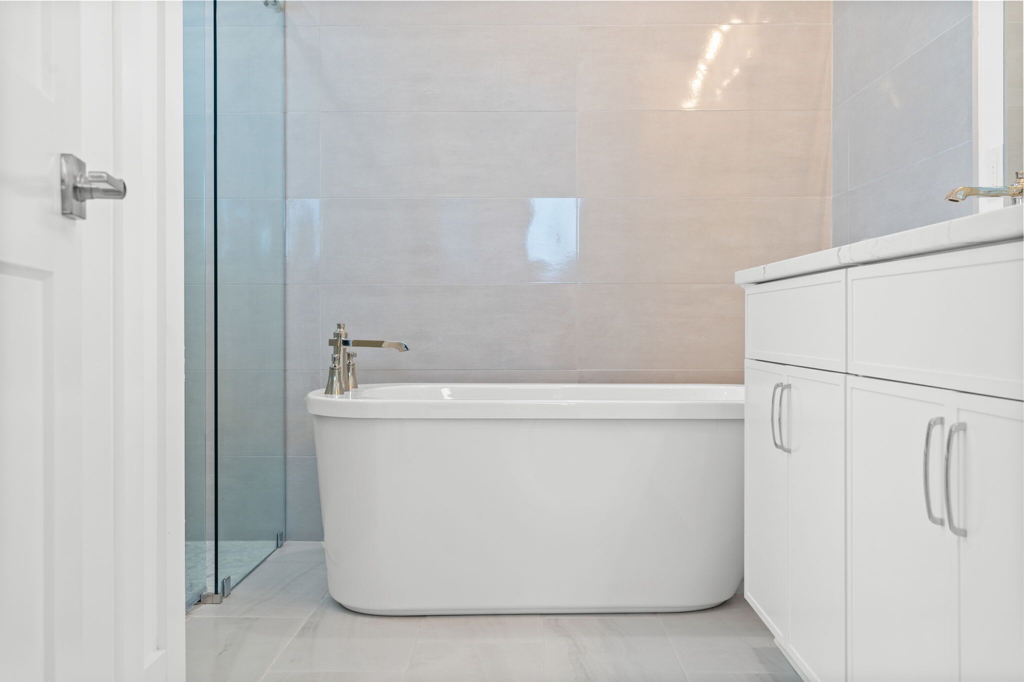 A modern bathroom with a freestanding bathtub, a glass shower enclosure, and white cabinetry.