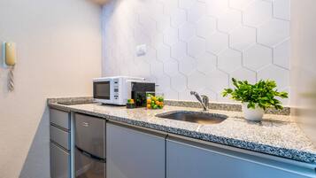 Una cocina funcional con microondas, pileta y planta en maceta.