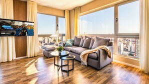 Un salon spacieux avec une grande fenêtre, un canapé, une table basse et un téléviseur fixé au mur.