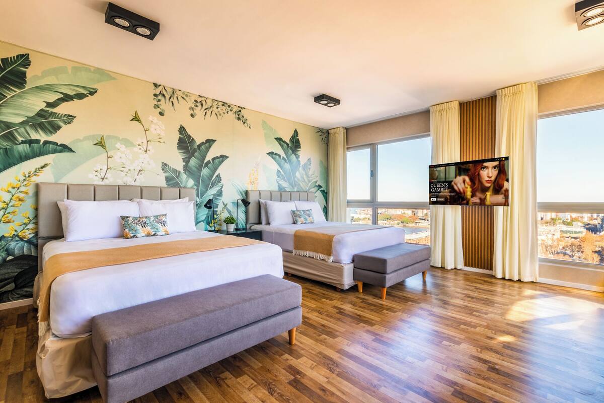 Une chambre d’hôtel avec deux lits, une télévision et une grande fenêtre donnant sur la ville.