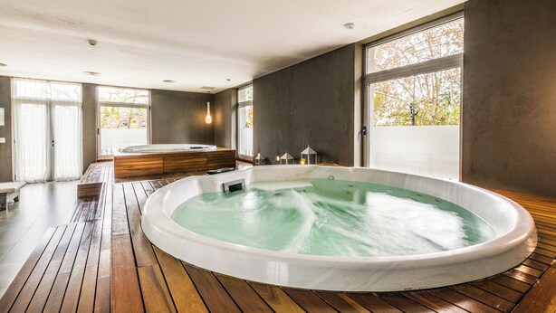 Un espace de bien-être moderne doté d’un grand jacuzzi, d’un plancher en bois et de grandes fenêtres laissant entrer la lumière naturelle.