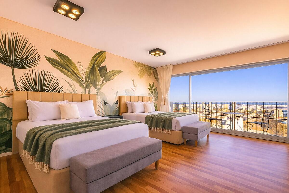 Une chambre moderne avec deux lits, un balcon offrant une vue sur la ville et une grande fenêtre.