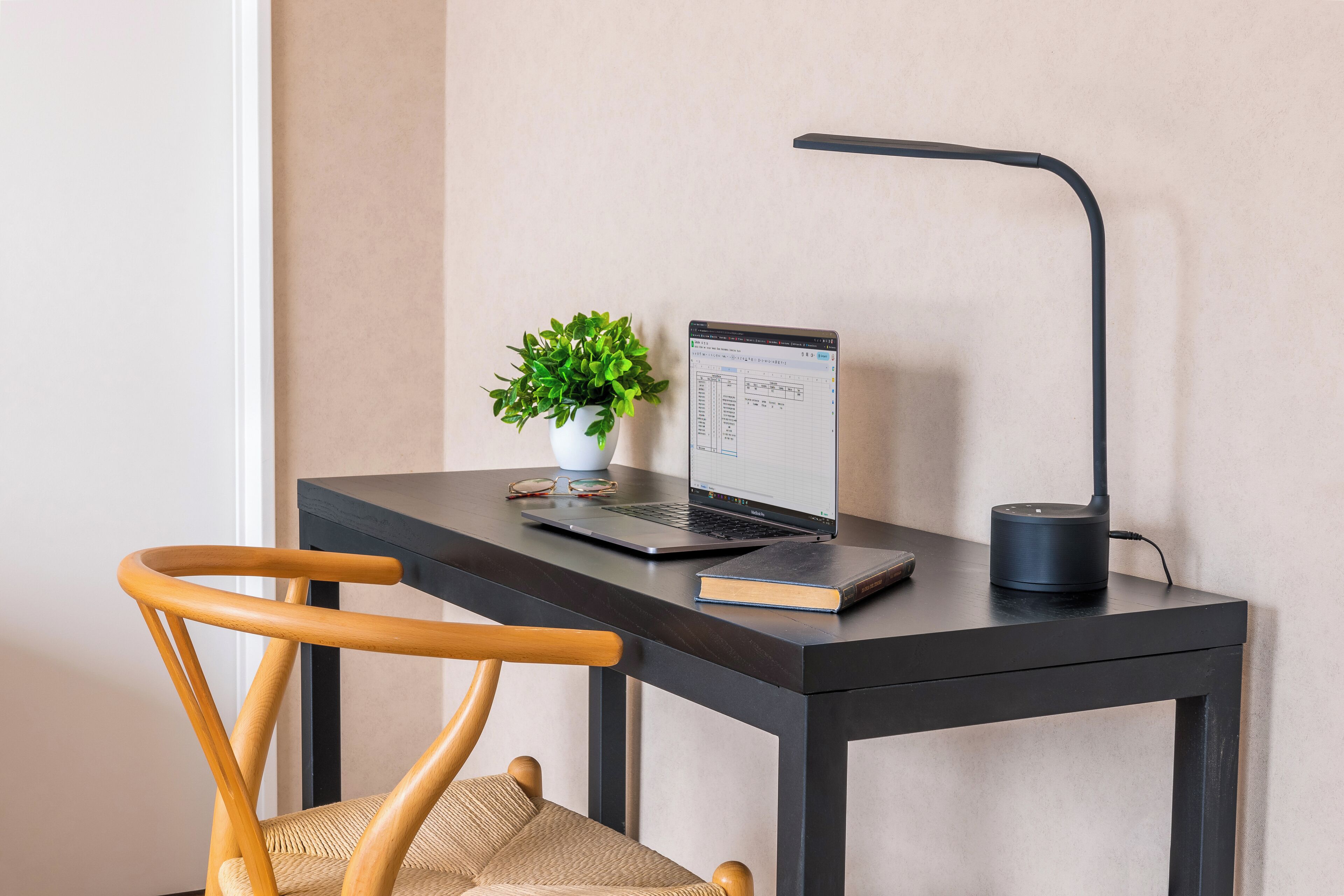 Un espace de travail avec un ordinateur portable, une plante et une lampe sur une table sombre.