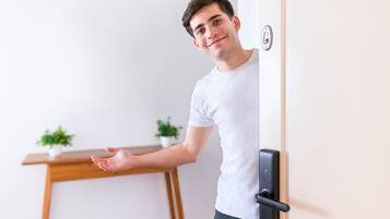 A person standing at a door with a modern handle, a wooden desk, and two potted plants in the background.