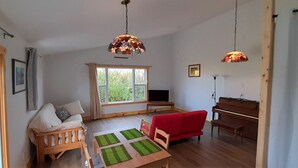 A cozy living room with a wooden sofa, a red couch, a dining table with green placemats, and a television on a stand. - Red Barn Bed & Breakfast (Lunenburg)