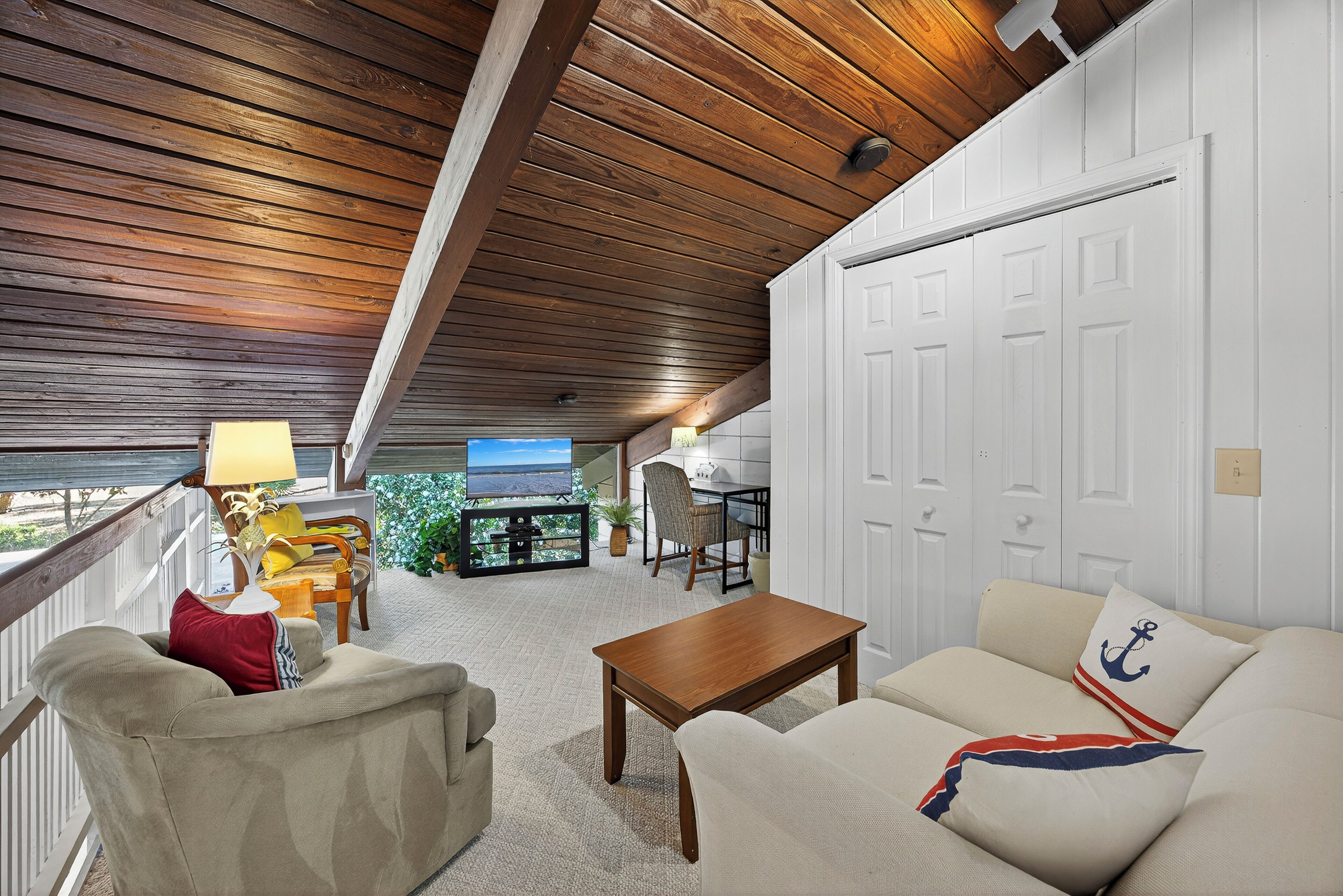 A cozy living room with a wooden ceiling, a white door, and a television in the background.