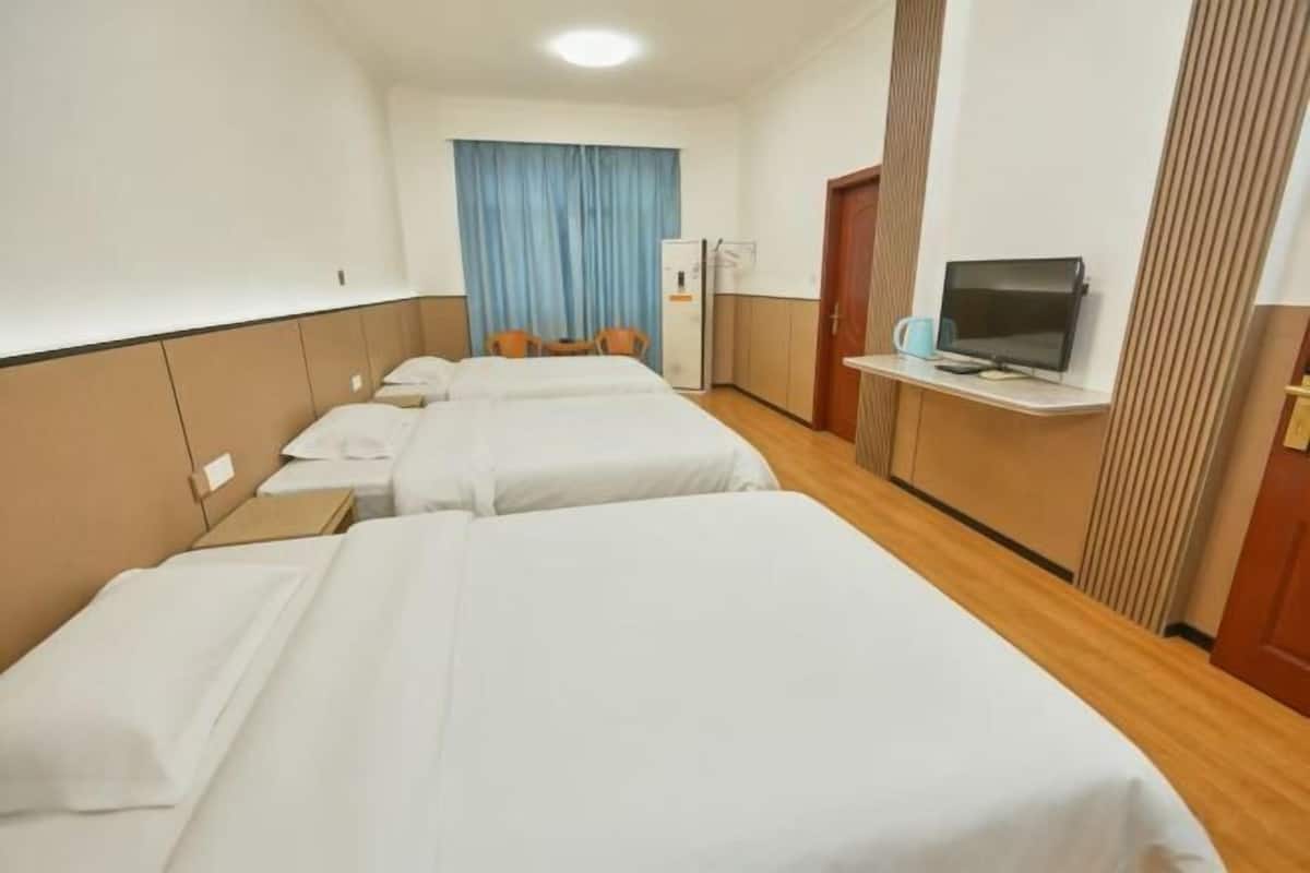 A hotel room with three beds, a television, a desk with a chair, and a window with curtains.