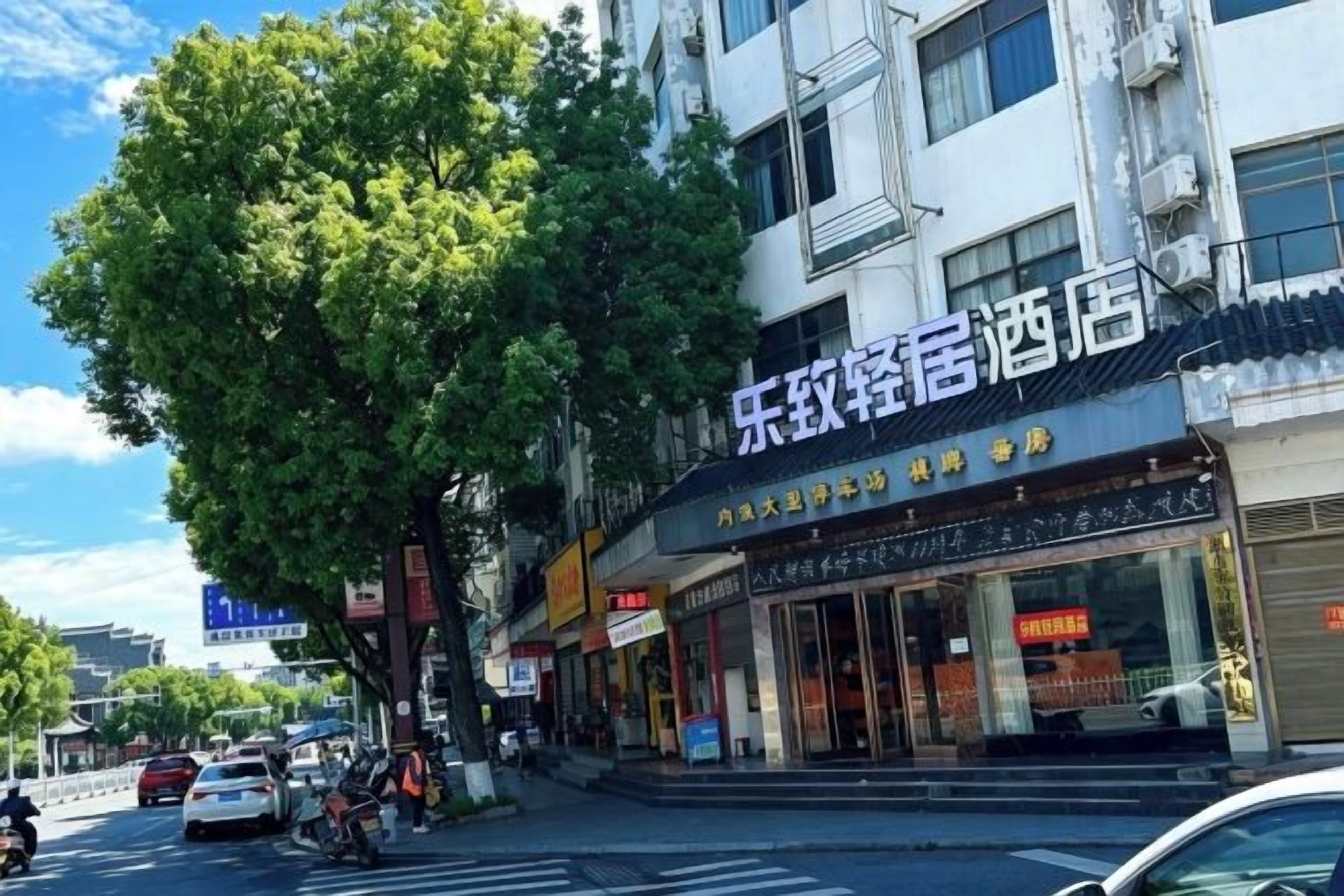 A hotel with a storefront featuring signage in a foreign language, a pedestrian crossing, and parked vehicles.