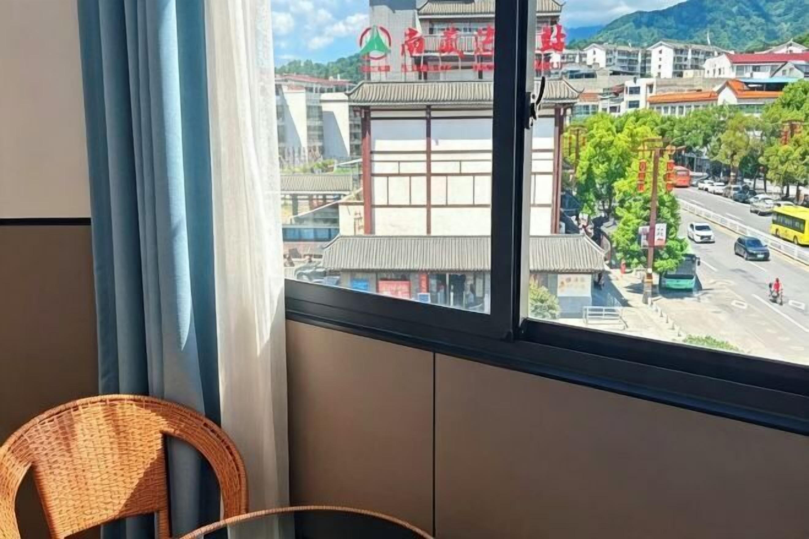 Vista desde una ventana con una silla de mimbre, un edificio con techo rojo y una calle con vehículos.
