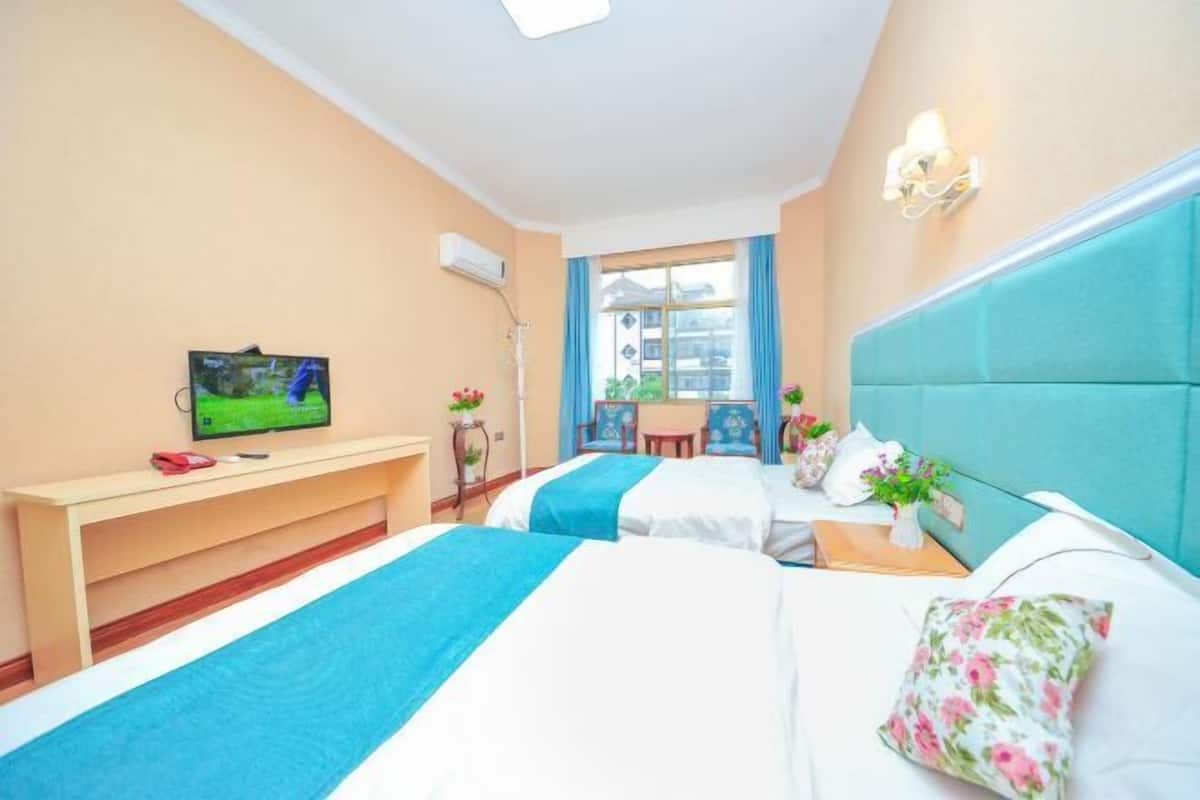 A hotel room with two beds, a TV on a stand, a desk, and a window with curtains.