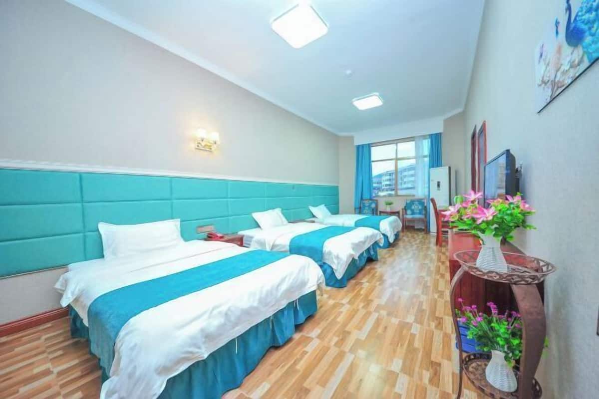 A hotel room with two beds, a wooden floor, a window, a desk, and a vase with flowers.