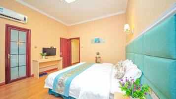 A bedroom with a bed, bedside table, and a desk with a chair. There is a door and an air conditioning unit on the wall.