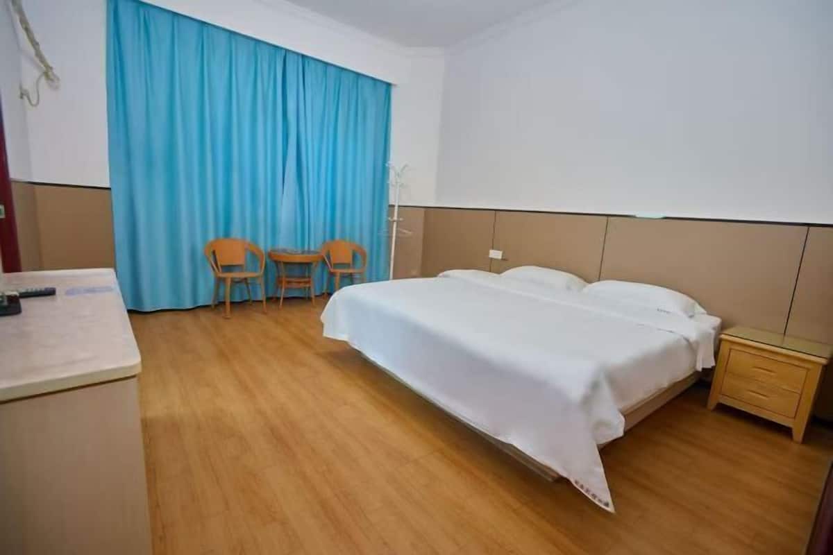 A hotel room with a bed, a desk, two chairs, a small bedside table, and a blue curtain.