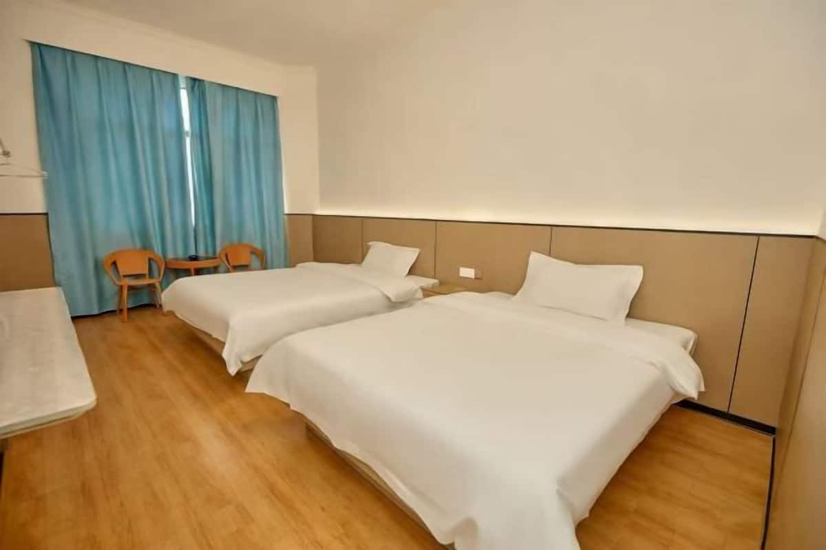 A hotel room with two beds, a small table, and a chair.