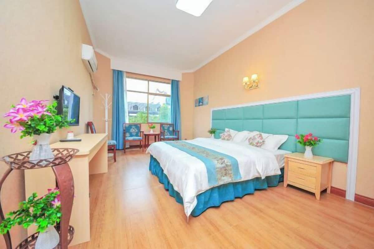 A bedroom with a bed, bedside table, desk, chair, and a window.
