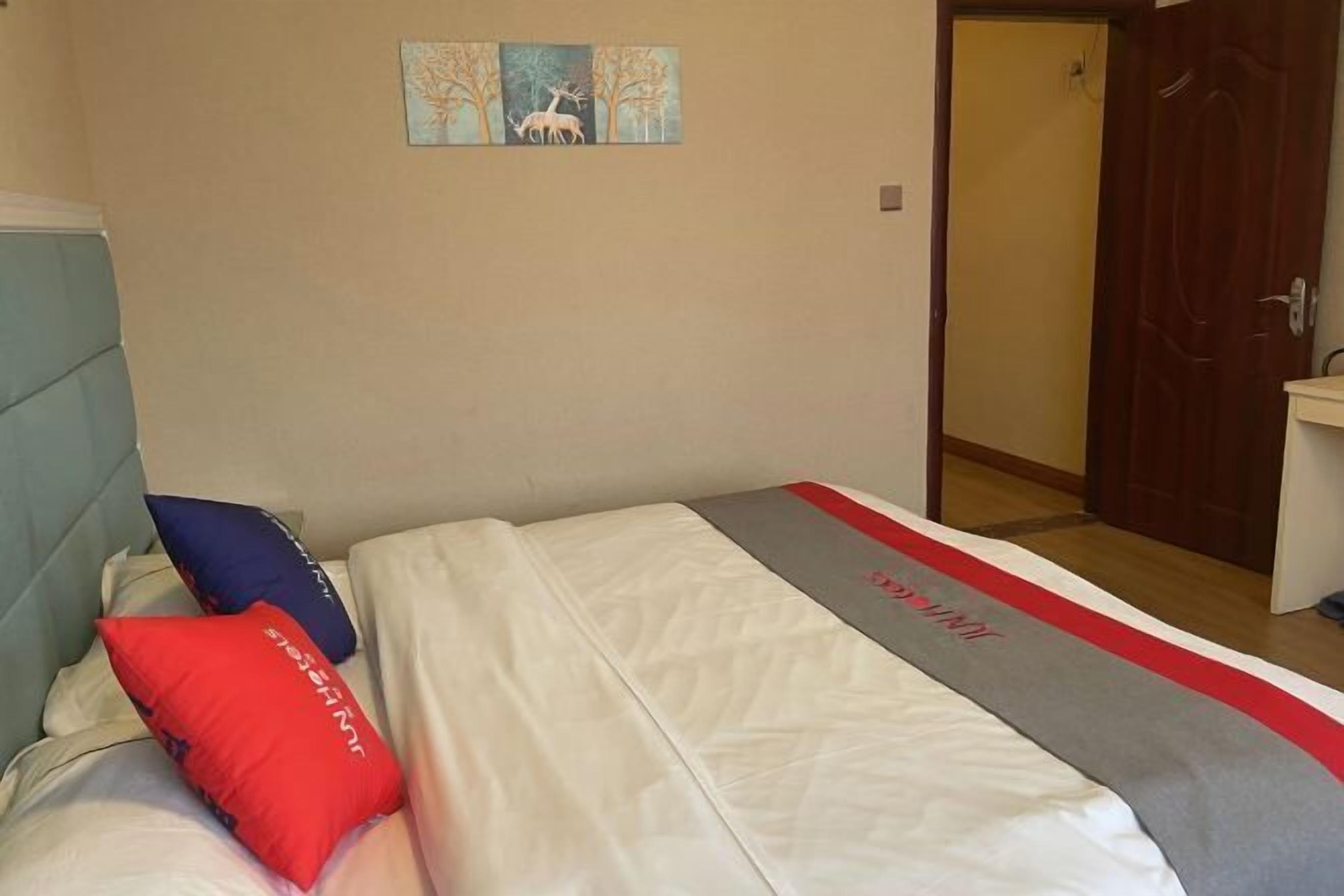 Una cama con una colcha blanca y roja, dos almohadas y un pequeño cuadro de ciervos en la pared.