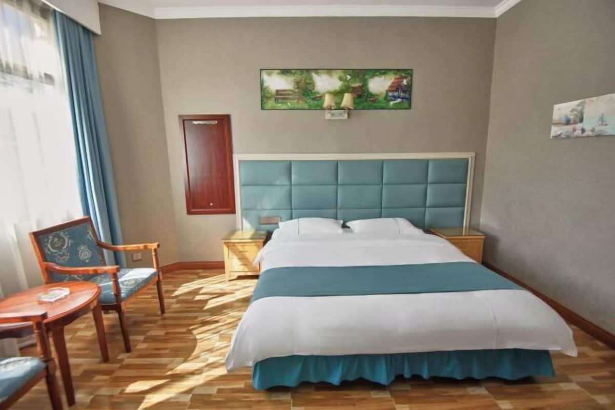 A hotel room with a bed, a chair, a nightstand, and a painting on the wall.