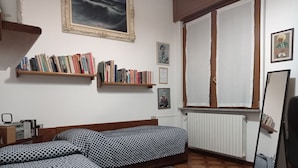 Een kamer met twee bedden, een boekenkast, een lijst en een raam met gordijnen.