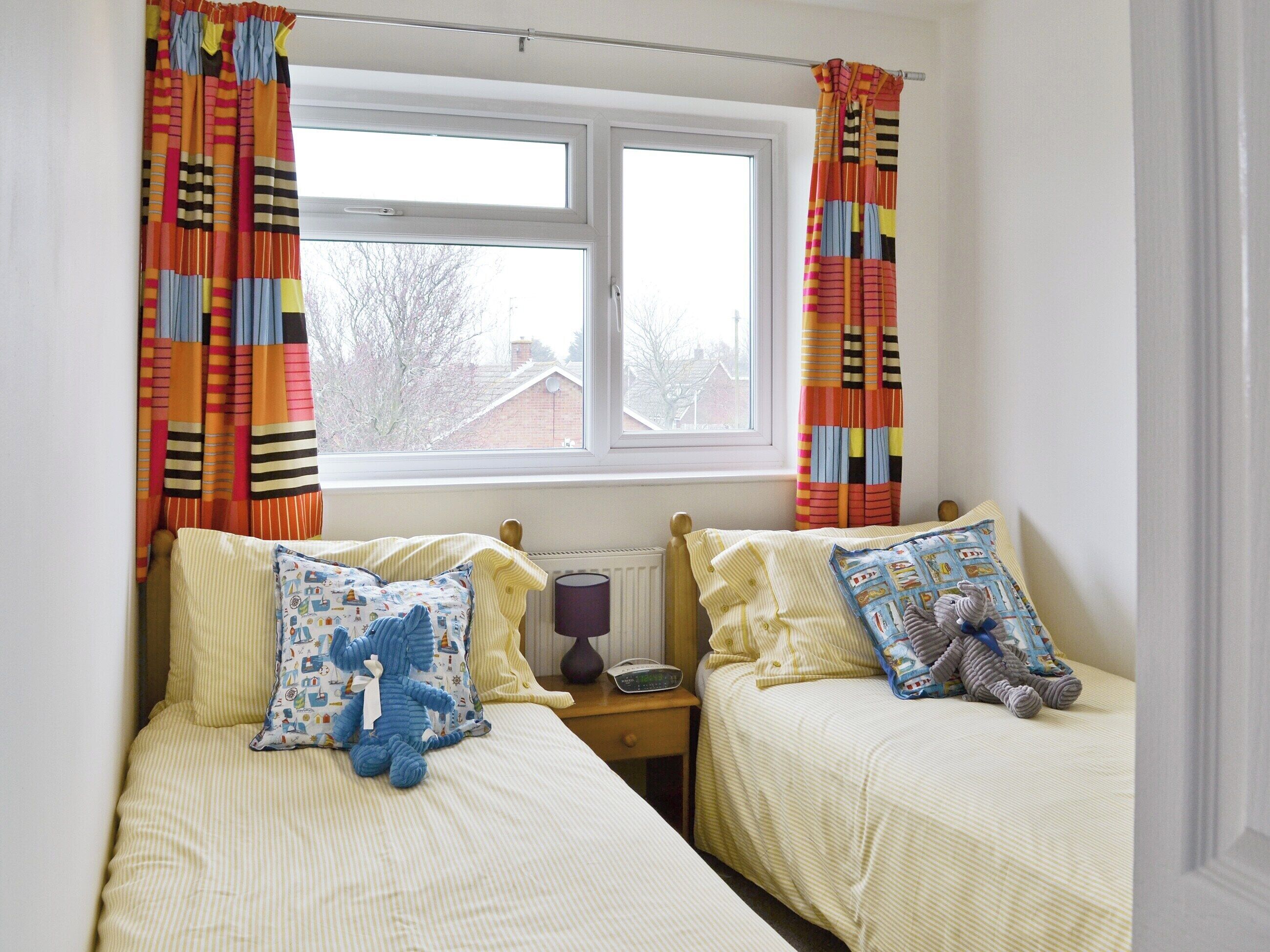 A bedroom with two single beds, a window, and curtains.