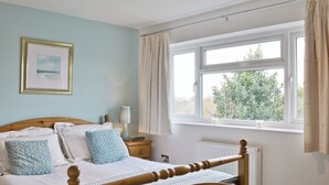 Ein Schlafzimmer mit einem hölzernen Bett, einem Nachttisch mit Lampe, einem gerahmten Bild an der Wand und einem Fenster mit Vorhängen.
