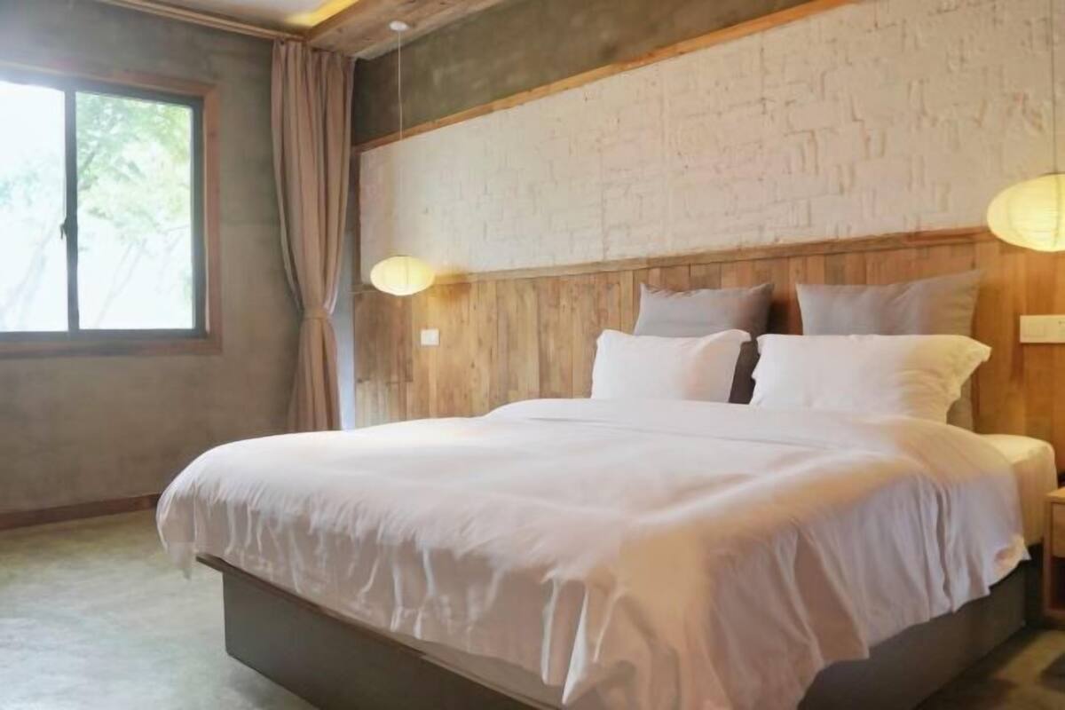 Een bed met een houten hoofdbord, een raam met gordijnen en twee wandlampen.