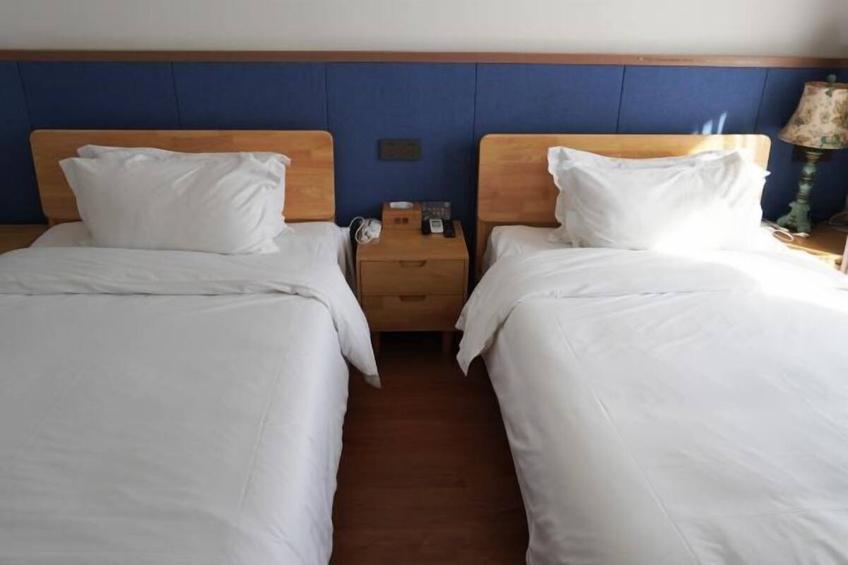 Een hotelkamer met twee eenpersoonsbedden, houten hoofdborden, een nachtkastje met een lamp en een kleine tafel met een telefoon en een doos.