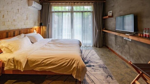 Une chambre d’hôtel avec un grand lit, un téléviseur posé sur une étagère et une fenêtre avec des rideaux.