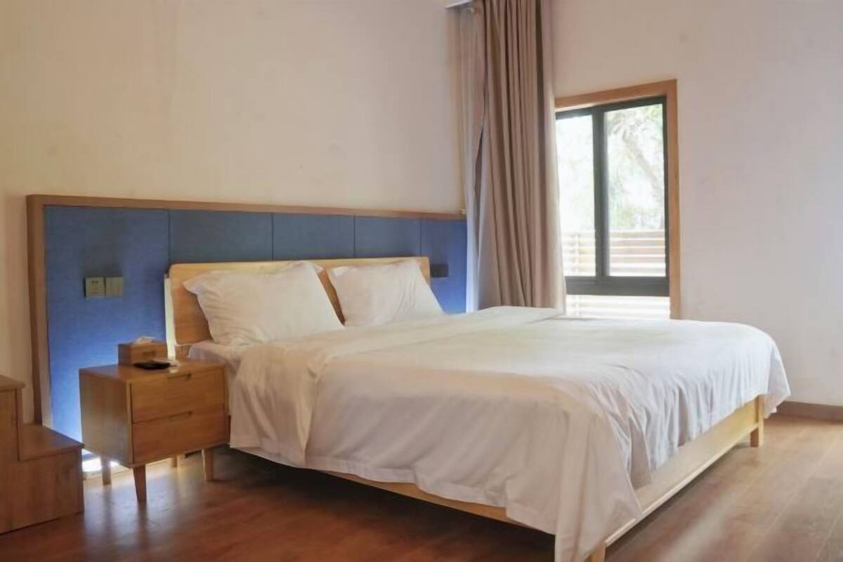 Een slaapkamer met een bed, een nachtkastje, een raam met gordijnen en een houten vloer.