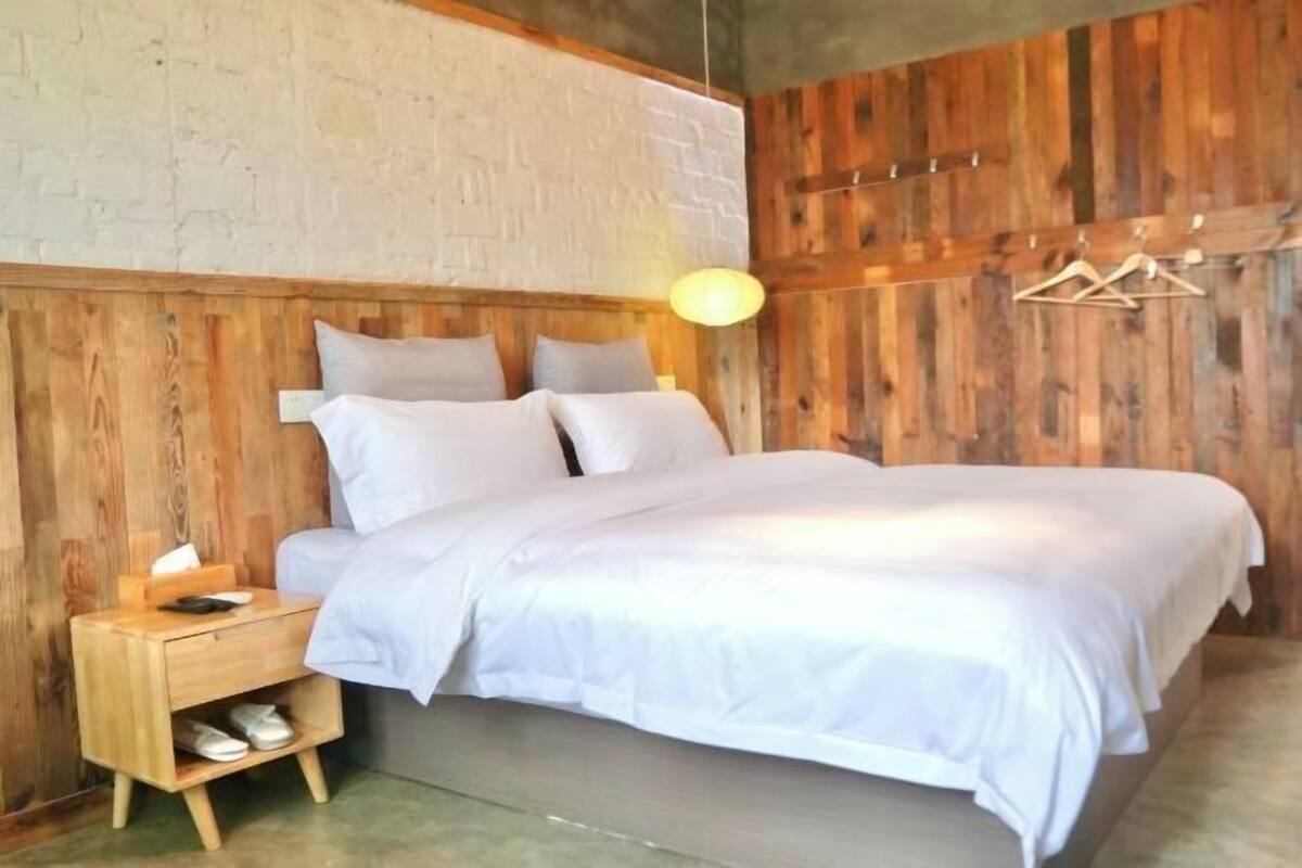 Een bed met wit beddengoed, een houten nachtkastje met schoenenrek en een hanglamp.
