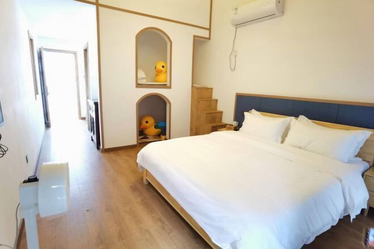 Een slaapkamer met een groot bed, een houten hoofdbord, een witte muur en een klein raam.