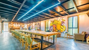 Une pièce spacieuse avec une longue table et des chaises, une fresque murale et un coin cuisine à l’arrière-plan.