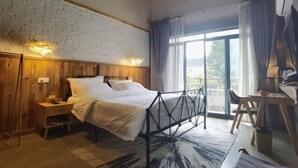 Une chambre à coucher comprenant un lit, une armoire en bois, un bureau, une chaise et une grande fenêtre avec des rideaux.