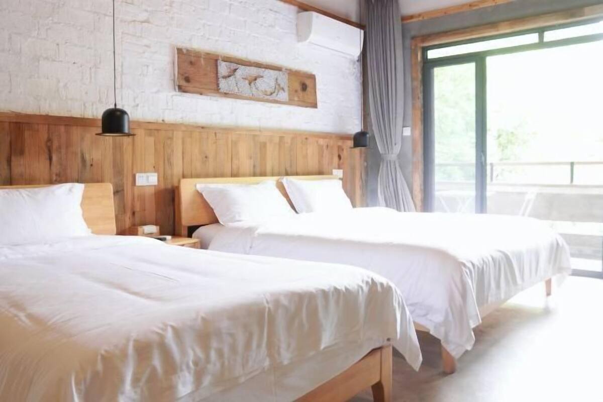 Een kamer met twee bedden, houten hoofdborden, een witte baksteenmuur en een groot raam.