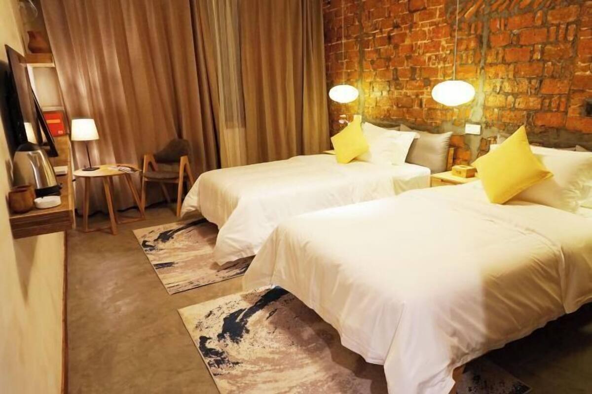 Een hotelkamer met twee bedden, een bakstenen muur, een tafeltje en een stoel.
