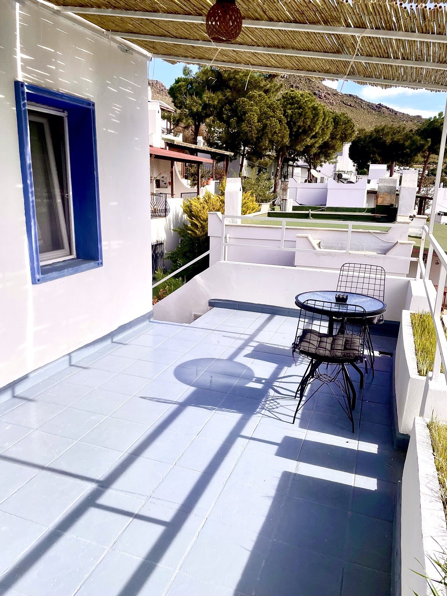 Un patio cubierto con piso de baldosas, una mesa con sillas y una ventana con detalles azules.