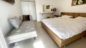 Un dormitorio con cama, sofá, televisor, espejo y estante en la pared con un cuadro.