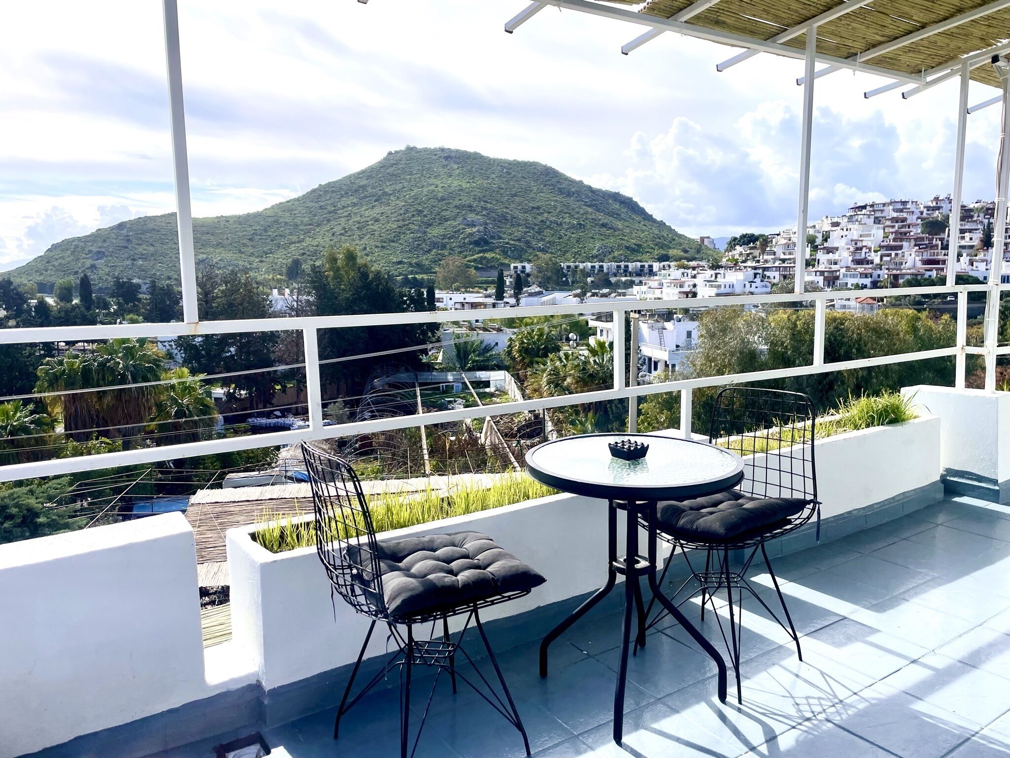 A balcony with two chairs and a table, overlooking a mountainous landscape and a town.