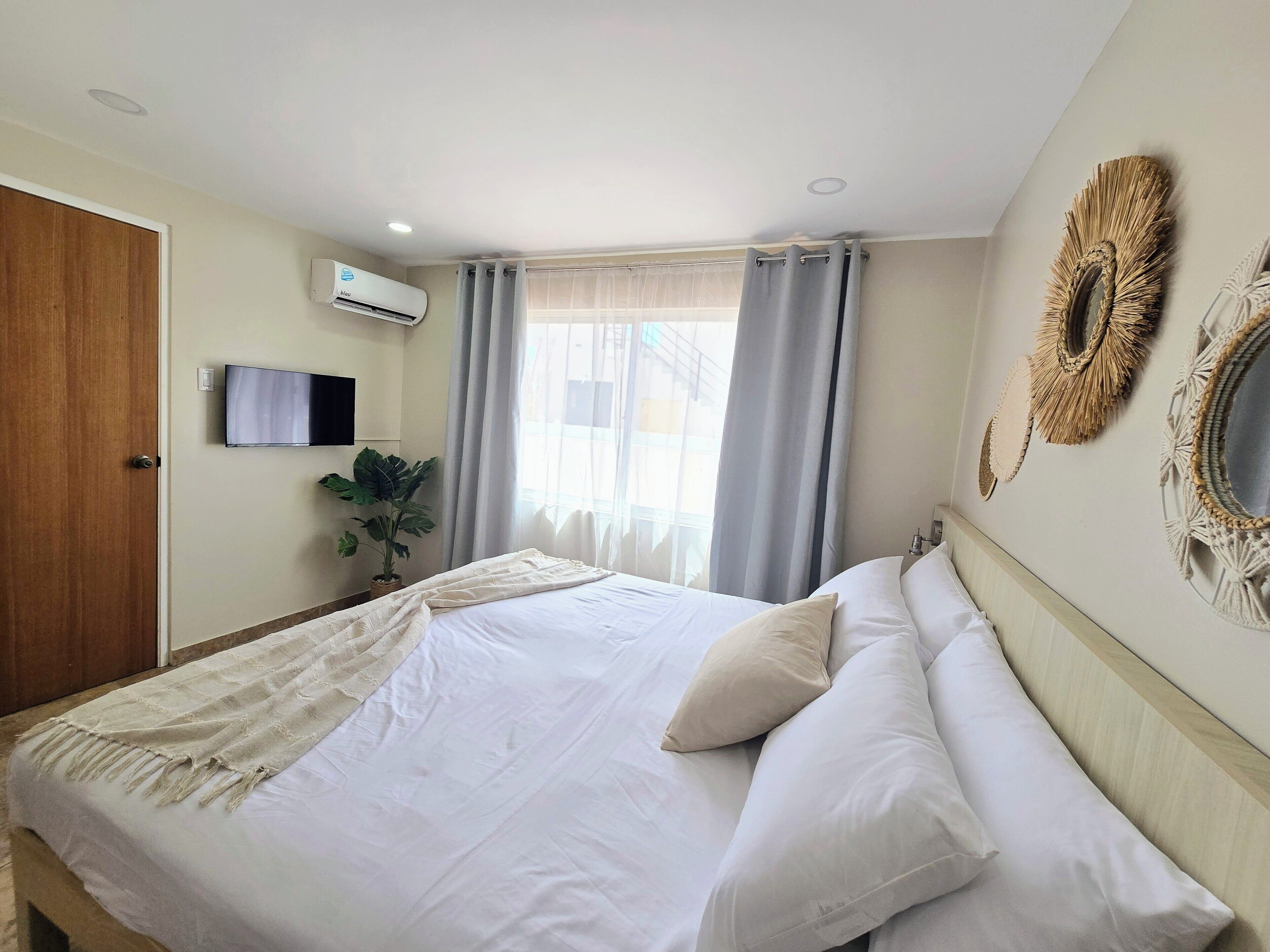 Ein Hotelzimmer mit einem Bett, einem Fernseher, einer Klimaanlage, einem Fenster mit Vorhängen und dekorativen Wandspiegeln.