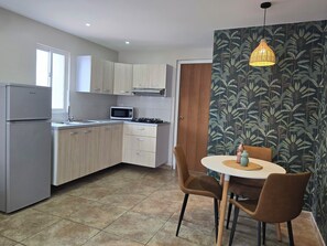 Une cuisine moderne équipée d’un réfrigérateur, d’un four à micro-ondes et d’une cuisinière, avec des armoires en bois et un coin repas comprenant une table et des chaises.