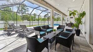 Eine Außenpatio-Terrasse mit Korbmöbeln, einem Pool und Blick auf Bäume und Himmel.