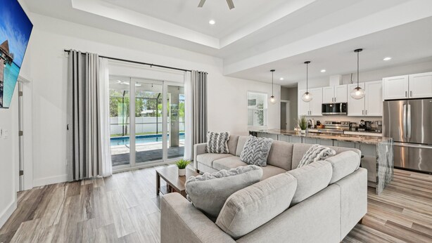 Ein großzügiges Wohnzimmer mit einer breiten Couch, einem Couchtisch und Blick auf einen Pool durch Glastüren.