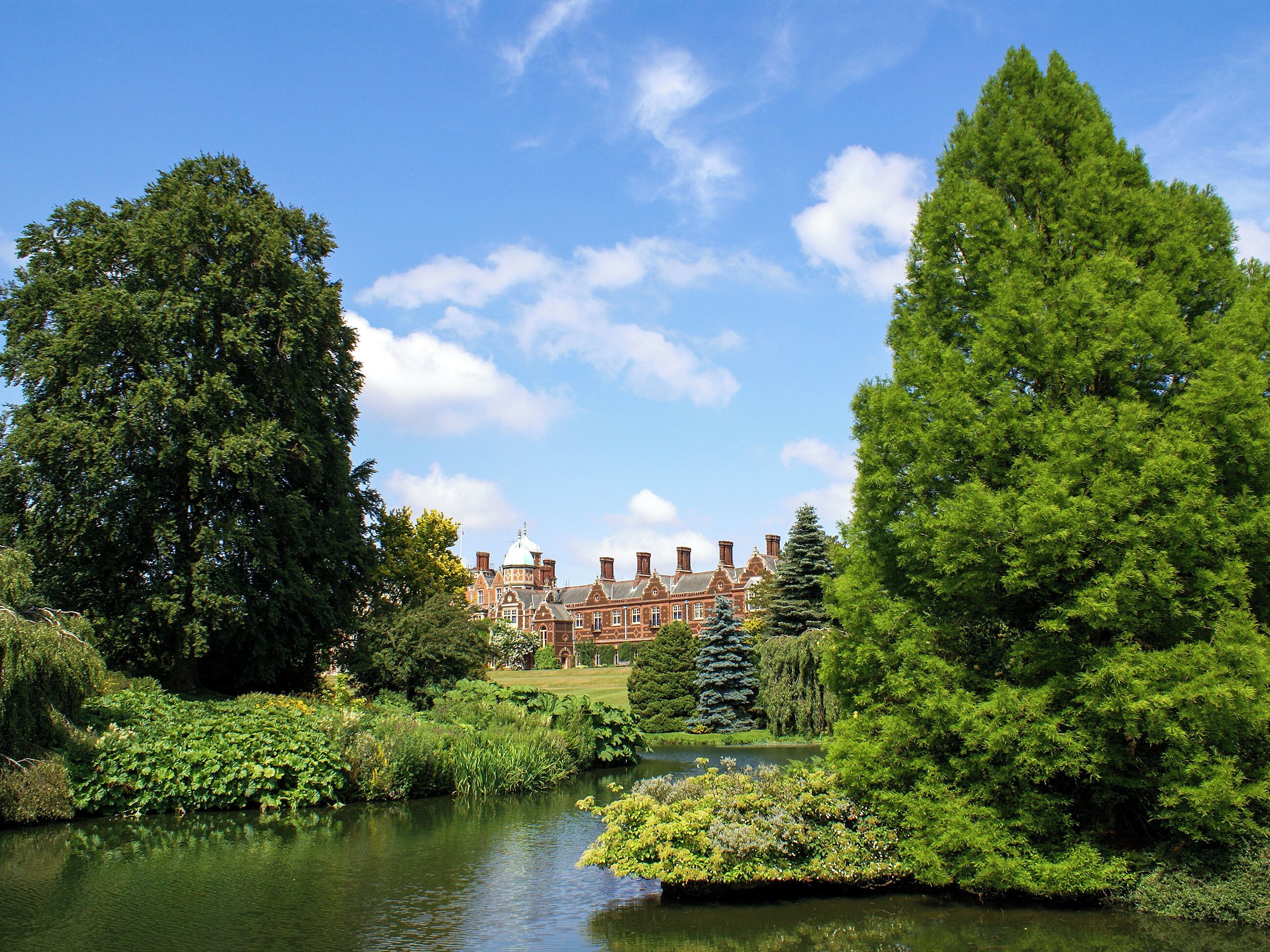 A large, historic building with a symmetrical facade and a central dome, surrounded by lush greenery and a calm water feature.