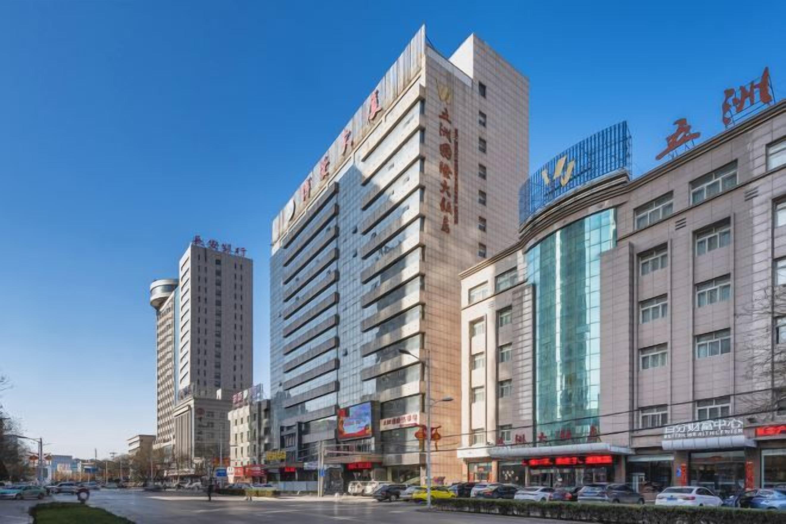 A multi-story building with commercial signage on the ground floor, a clear sky, and a street with parked cars.