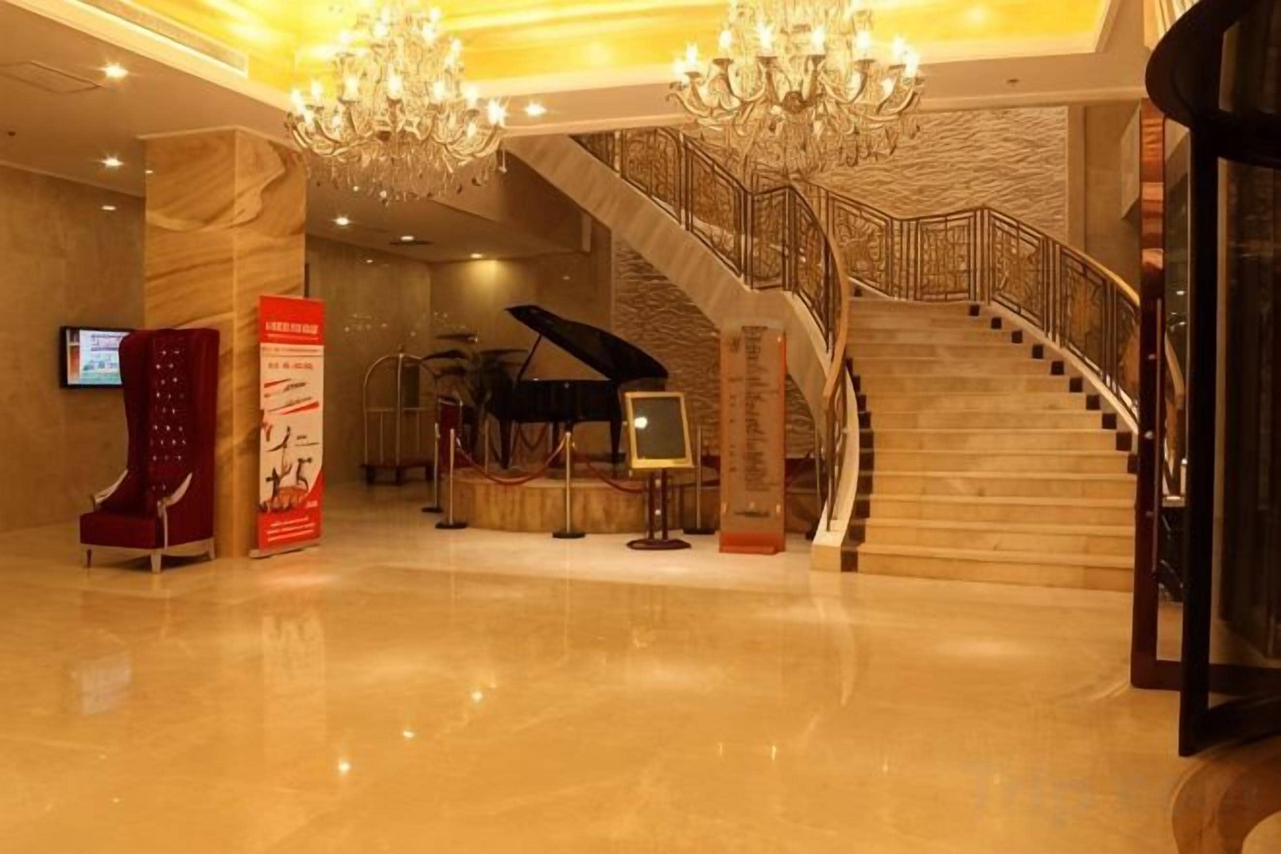 Un vestíbulo con una imponente escalera, un piano de cola y un candelabro.