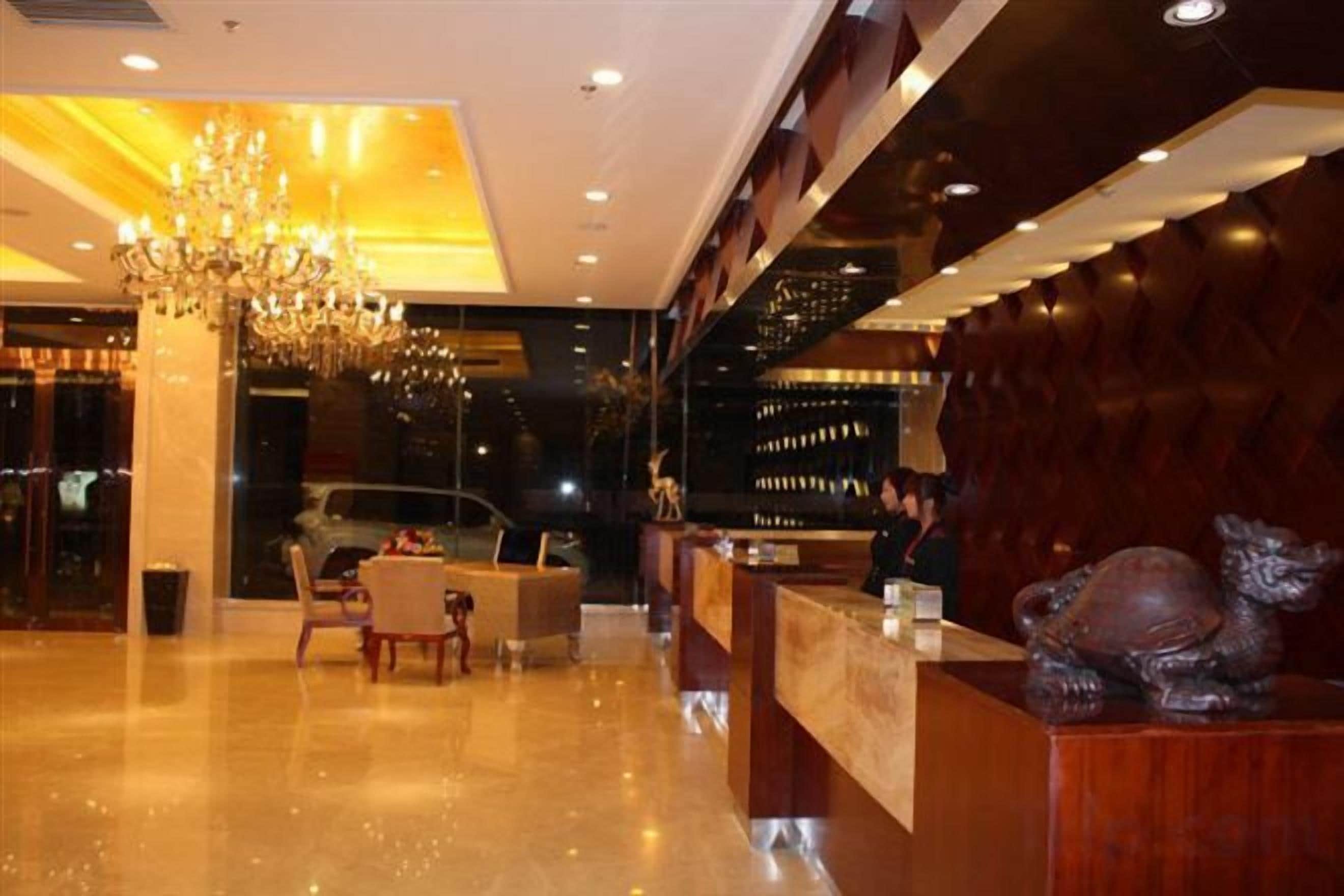 A hotel lobby with a reception desk, a chandelier, and a seating area.