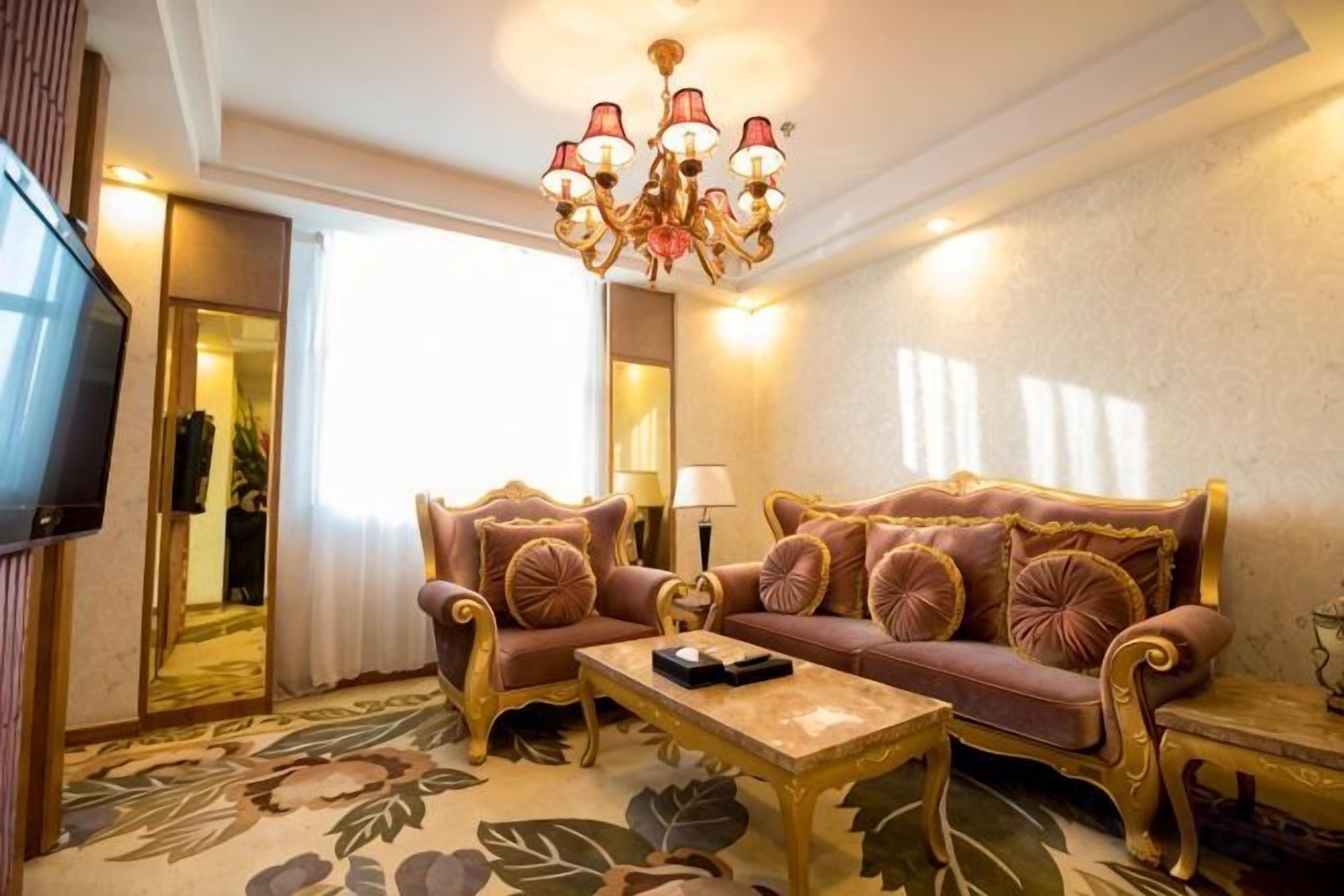 A room with a sofa, a coffee table, a TV, and a chandelier.