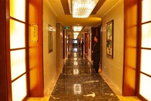 Um corredor de hotel com piso de mármore, painéis de madeira e um candelabro.