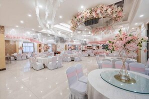 A spacious banquet hall with round tables and chairs, a central floral arrangement, and a chandelier.