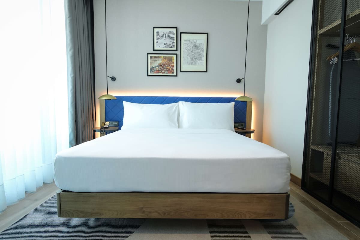 Ein ordentlich bezogenes Bett mit Holzrahmen, weißer Bettwäsche, einem blauen Kopfteil und zwei gerahmten Bildern an der Wand darüber.