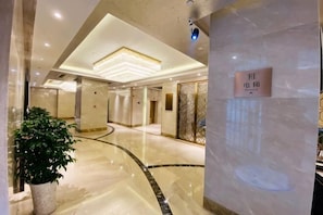 A hotel lobby with a marble floor, a potted plant, a sign with Chinese characters, and a modern ceiling design.